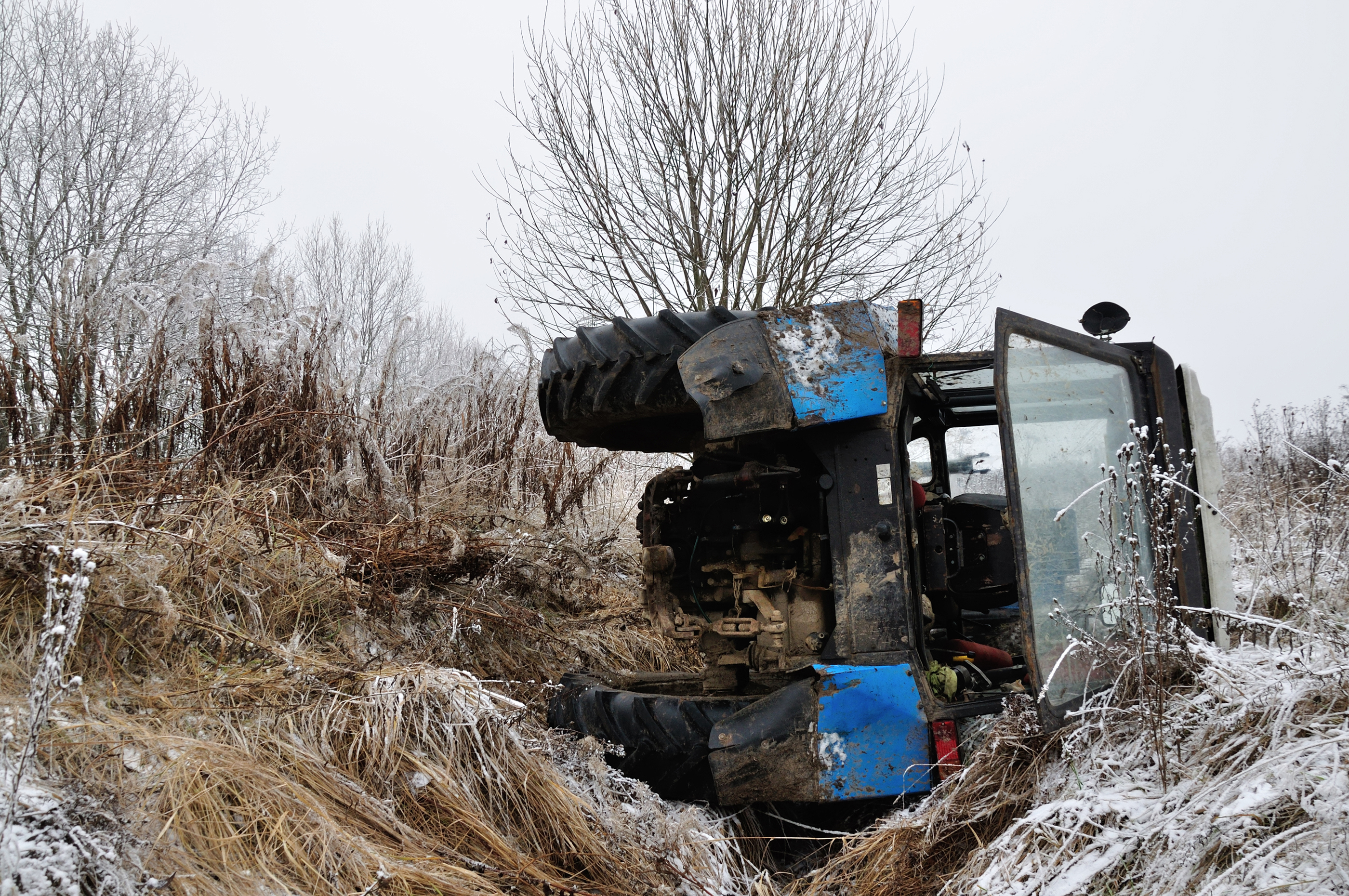 Blue tractor crashed on its side due to a farm accident.