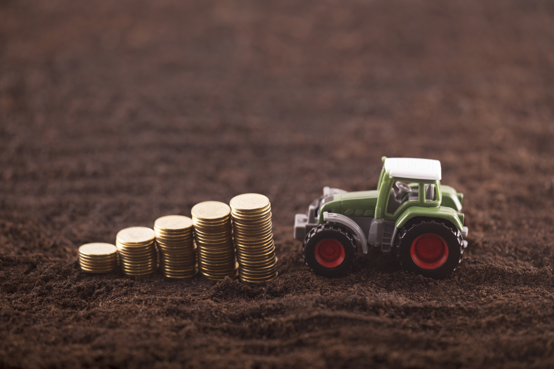 Green toy tractor carrying coins on a soil field