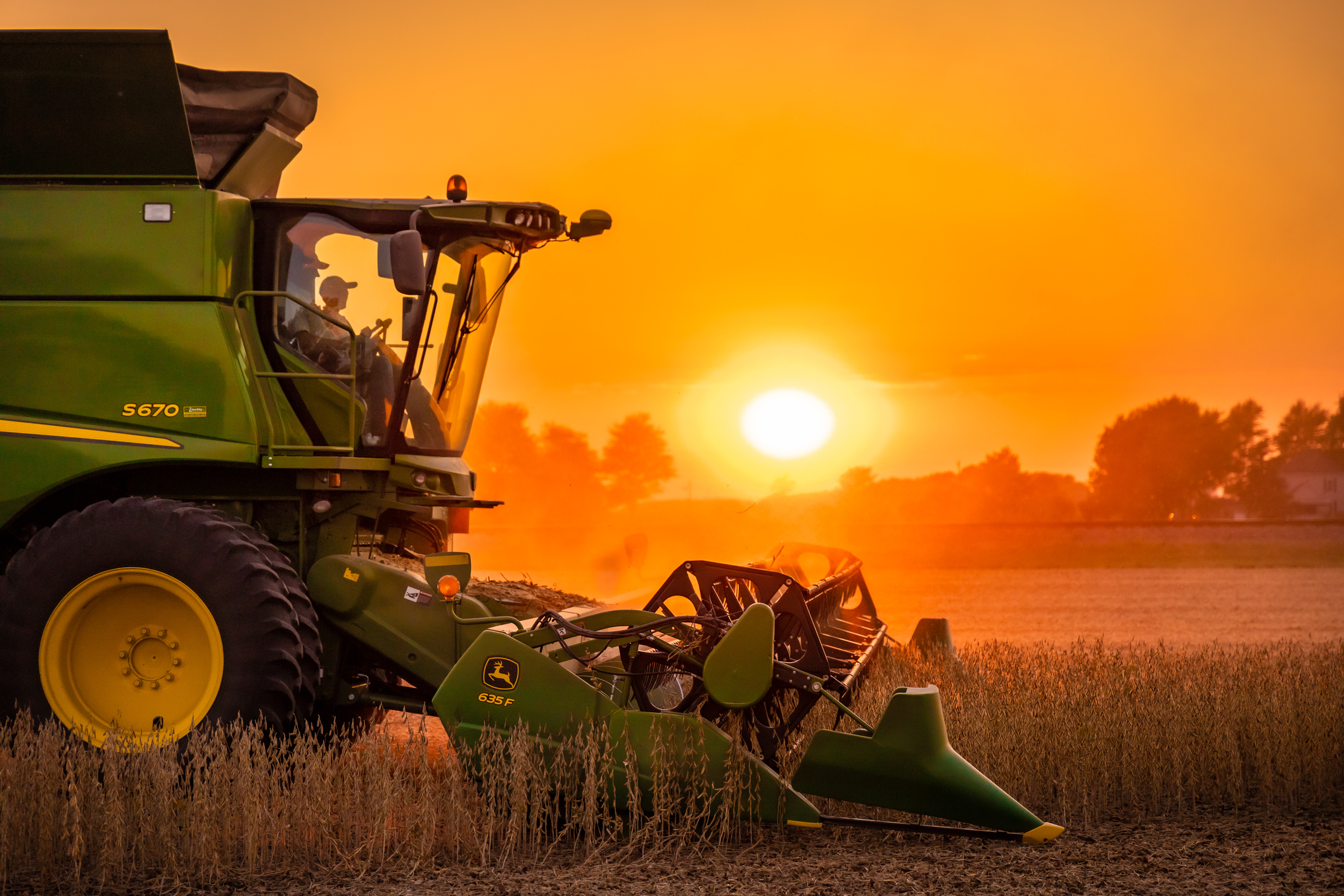 Farmer on green harvesting machinery as the sun sets
